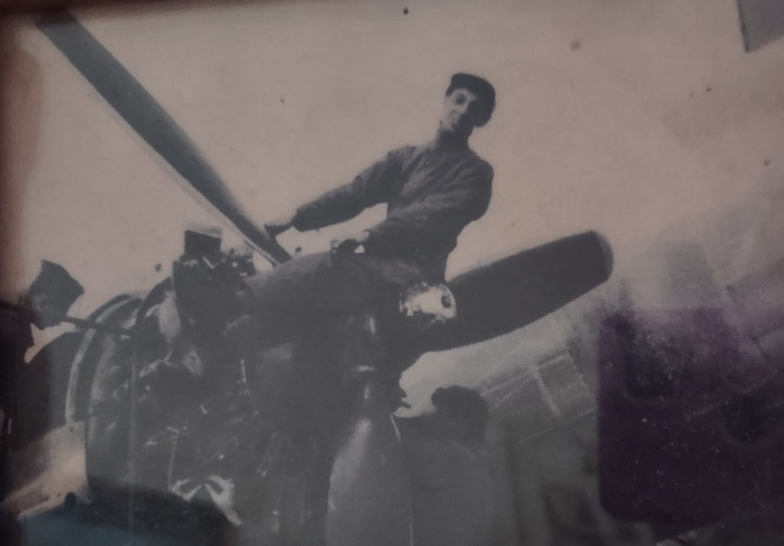 A young man climbs on the front propellor of a WWII plane