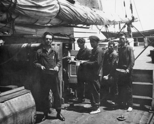 Black and white photo of whalers standing in line with plates on deck