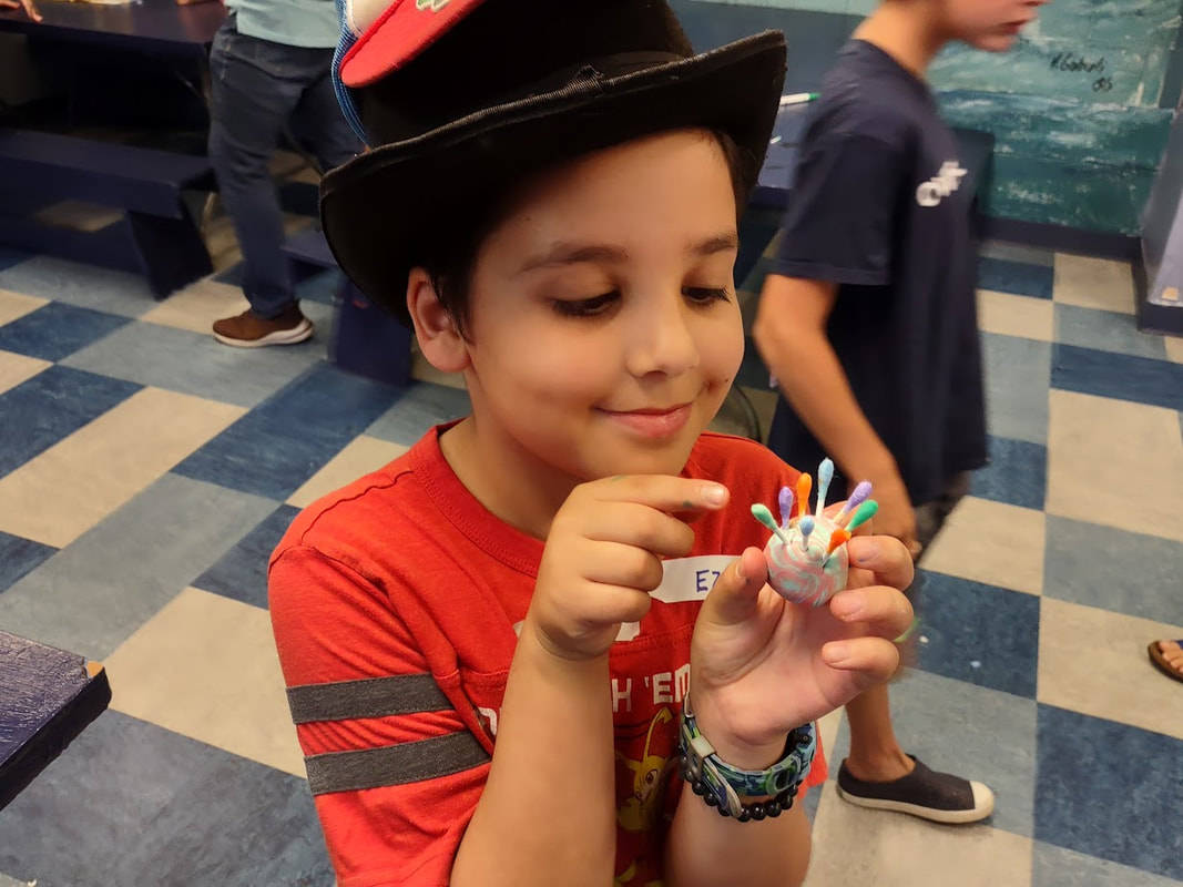 A boy in a top hat smiles and points to his urchin craft made from q tips