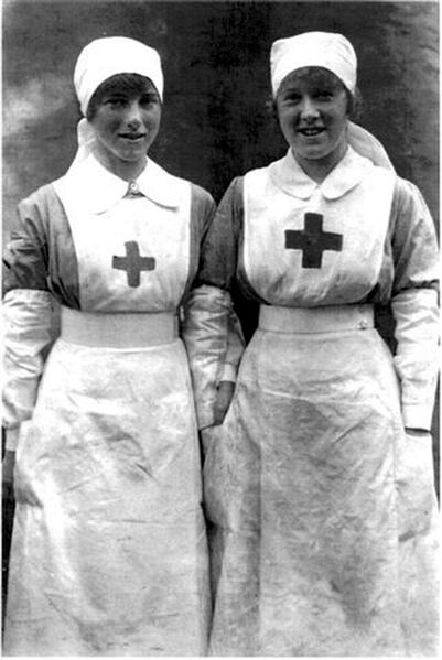 Two female caucasian nurses in red cross uniforms pose and smile wearing aprons
